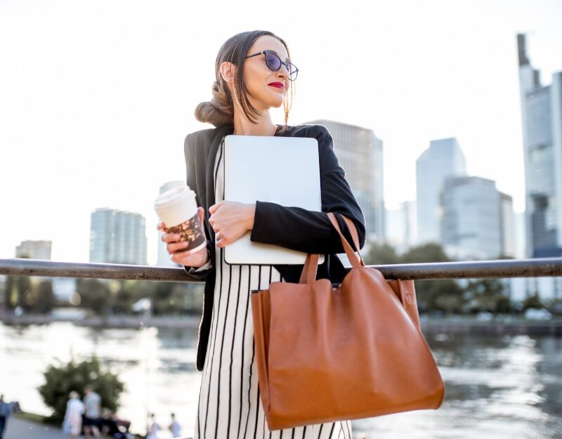 Businesswoman oh her way to work, and holding her coffee, laptop, and a possibly tax-deductible handbag