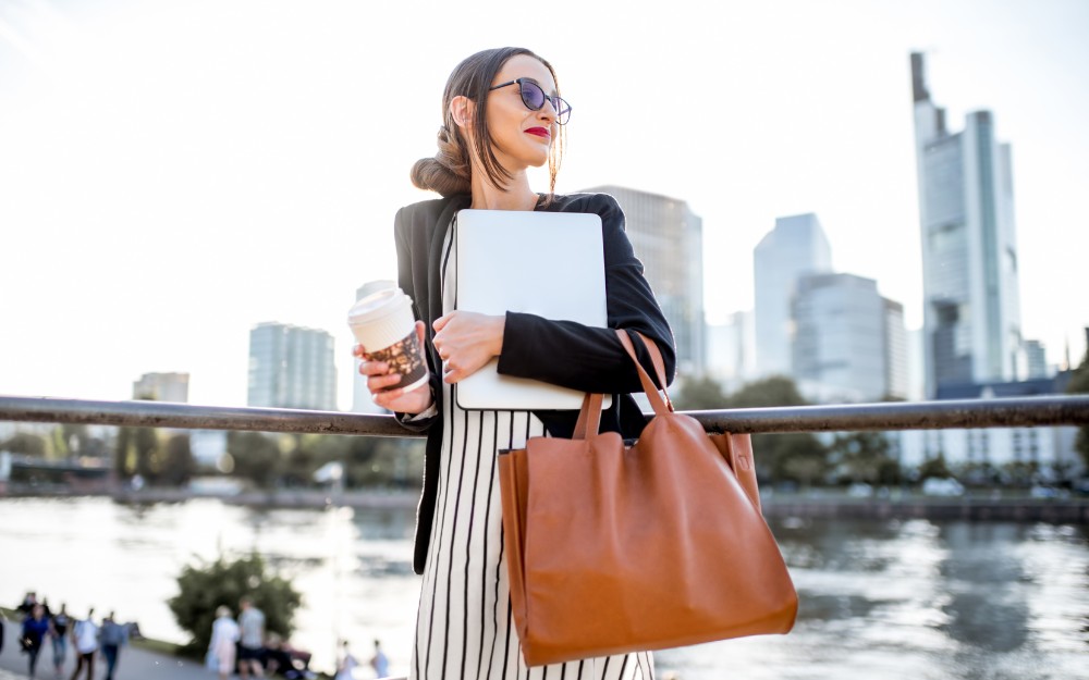 Businesswoman oh her way to work, and holding her coffee, laptop, and a possibly tax-deductible handbag