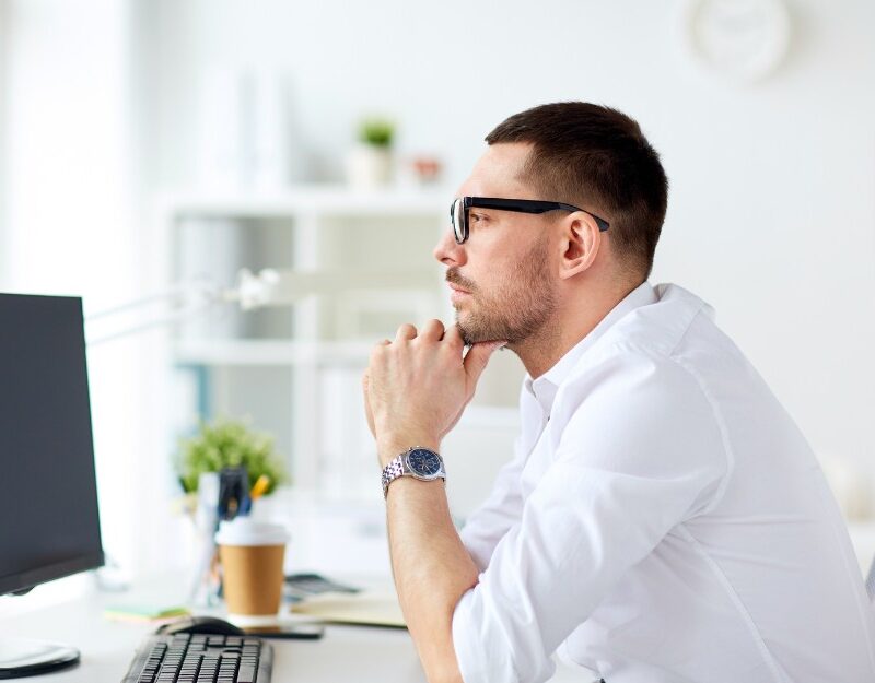 Pensive businessman in front of computer thinking about whether to register for GST.