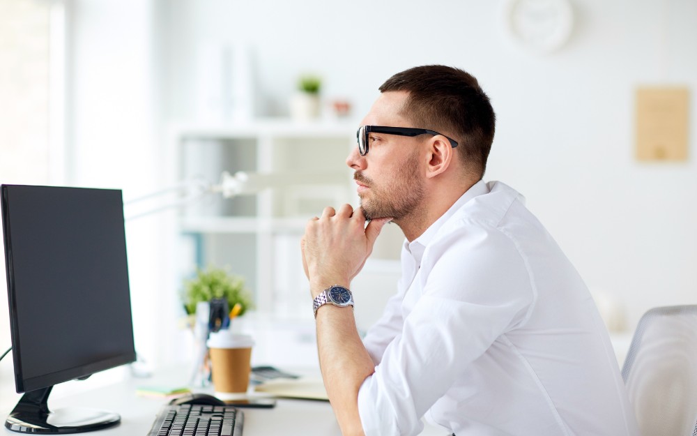 Pensive businessman in front of computer thinking about whether to register for GST.